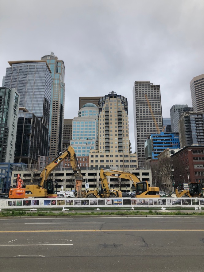 Many tall buildings behind construction equipment and a road